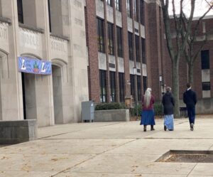 A small group walking along the sidewalk beside a school and praying