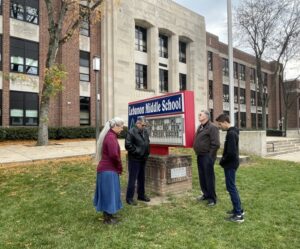 A small group people praying in front of a school building, gathered around its marquee sign