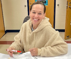 A school volunteer sits at a desk in a classroom.